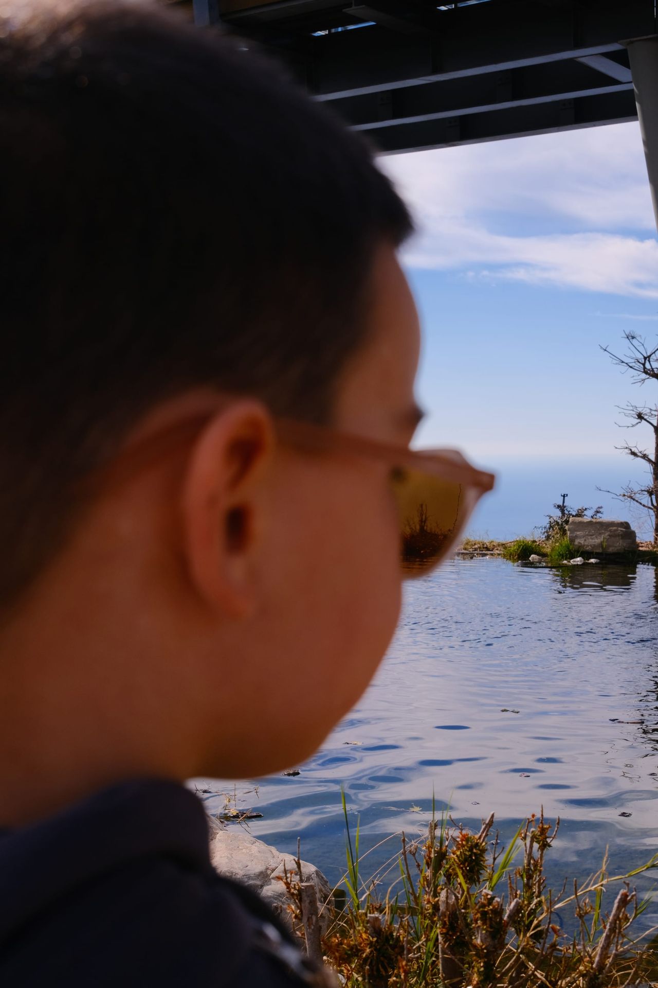Child in sunglasses looking across a small mountain pond
