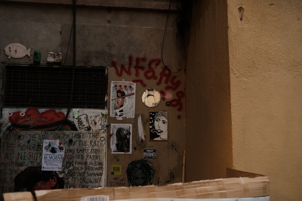 Weathered Barcelona doorway and wall covered in graffiti, pasted portraits and small posters.