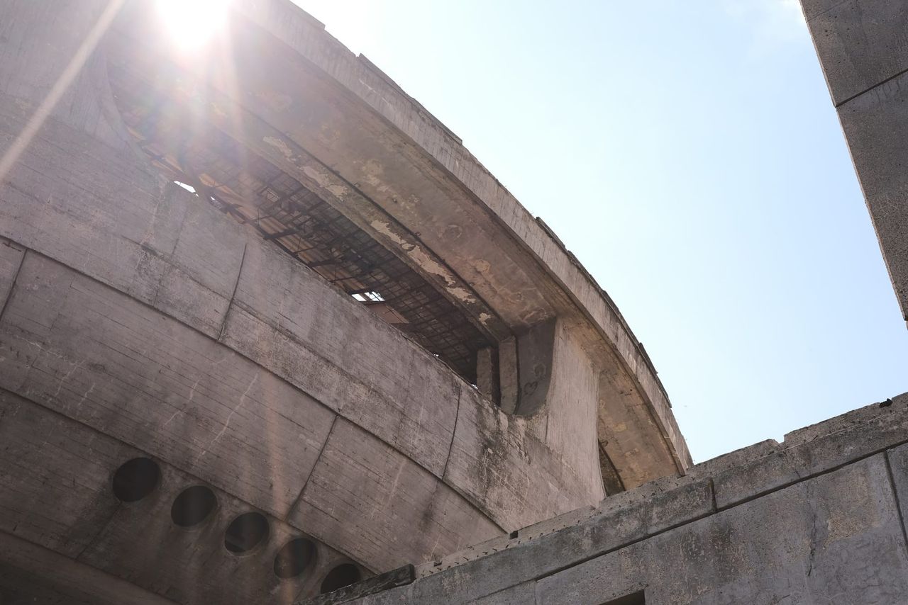 Sunlight flares over Buzludzha's weathered curved concrete rim and damaged windows.