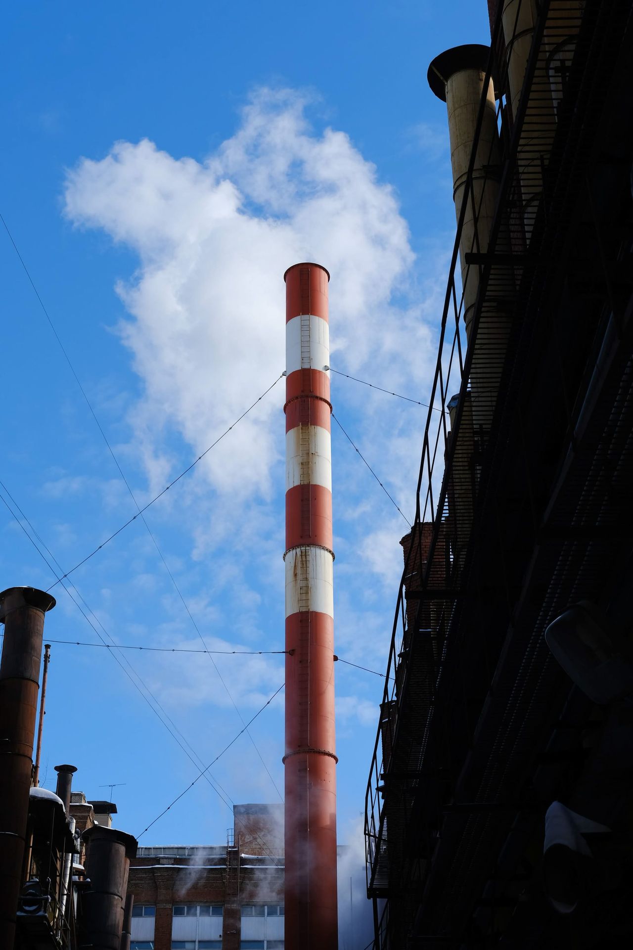 Red-and-white industrial chimney rising into a blue sky with white clouds in Moscow