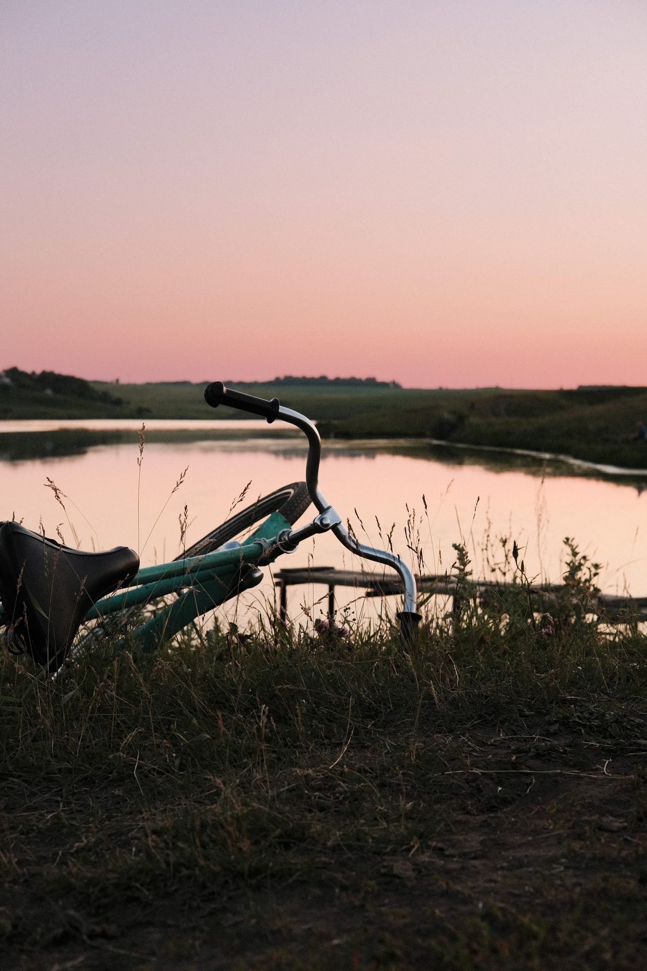 Bicycle beside a calm lake beneath a pastel pink and blue evening sky