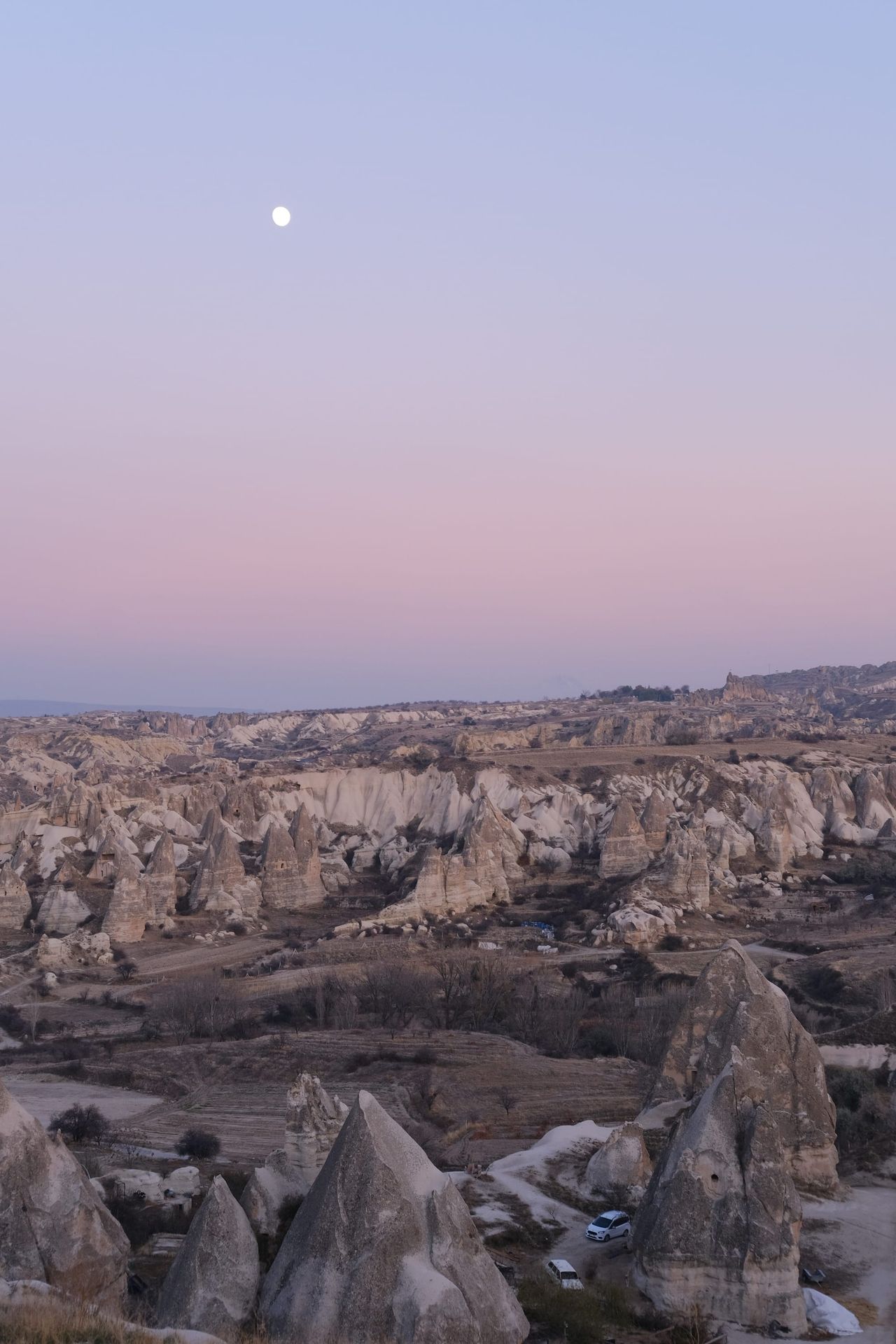 Moon above Cappadocia rock formations beneath a pale pink and blue twilight sky