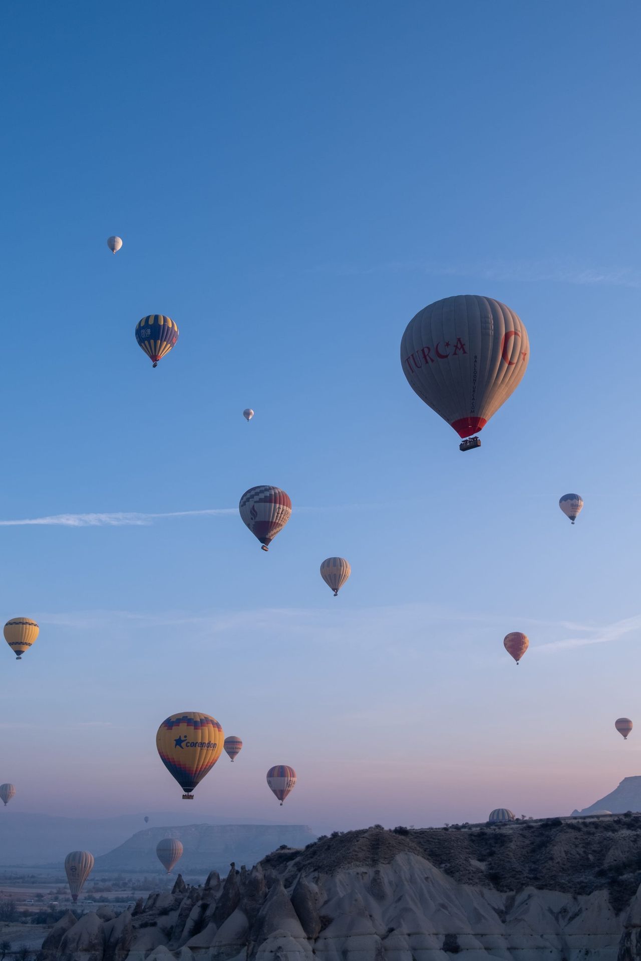 Hot-air balloons floating above Cappadocia under a clear blue dawn sky