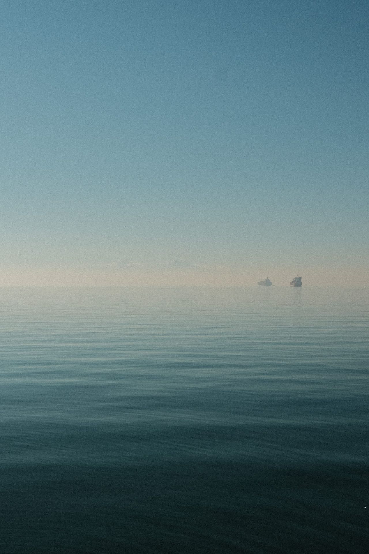 Calm Greek sea fading into a hazy blue horizon with two distant rocky islets