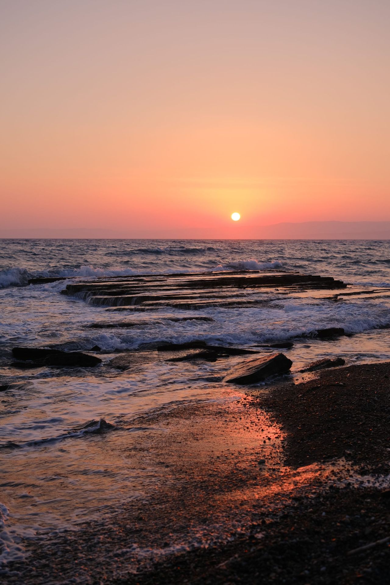 Orange sun setting over a rocky shoreline and gently breaking waves