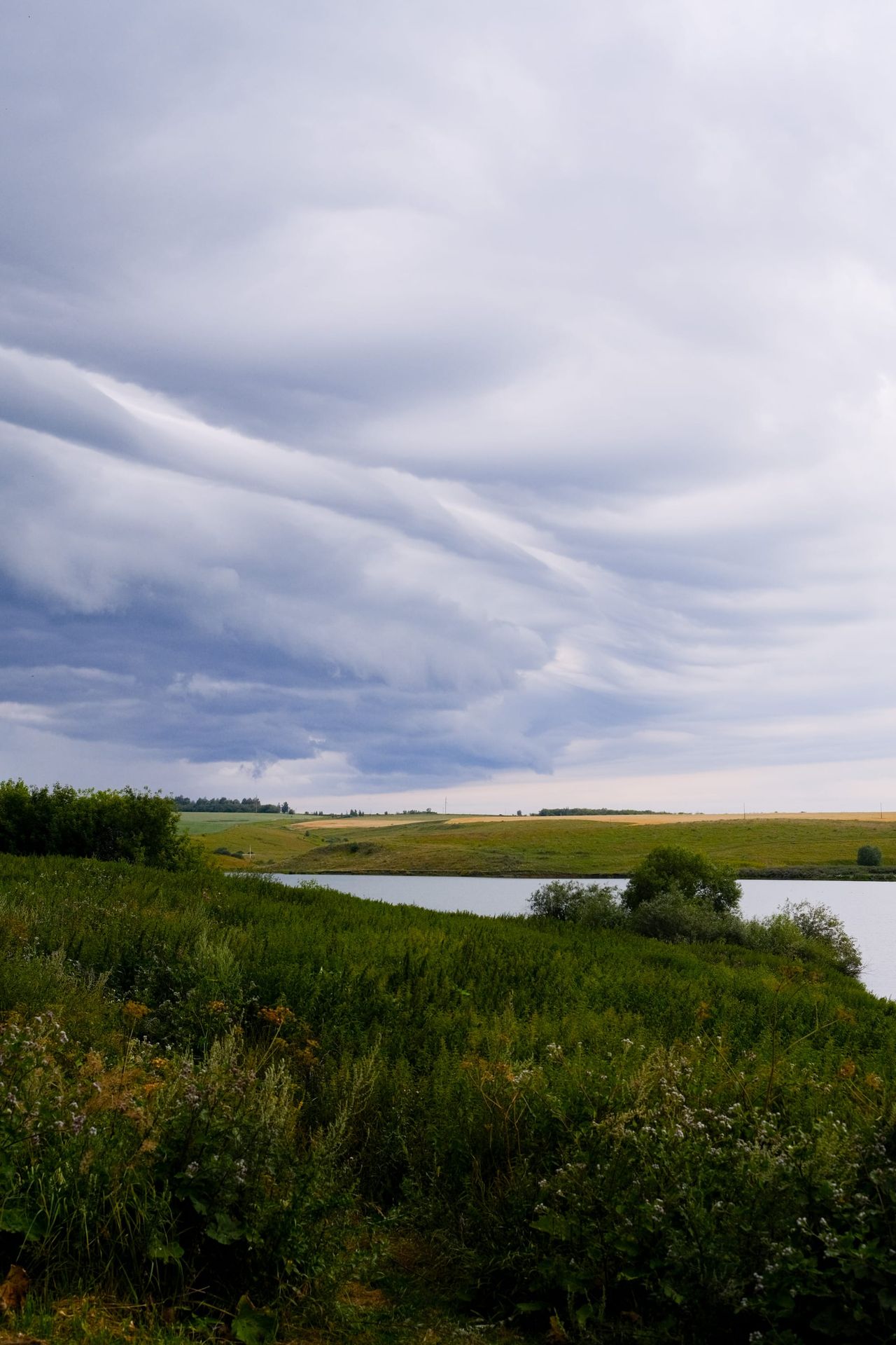 Layered shelf clouds sweeping over green wetlands and a winding river