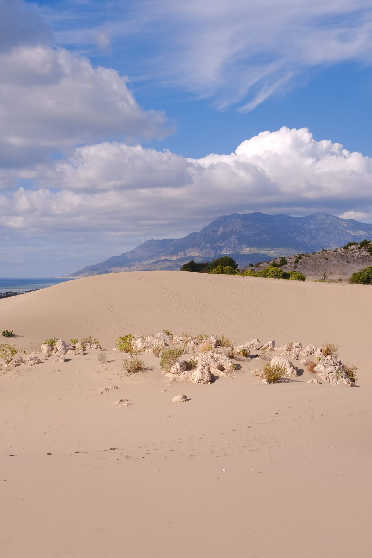 Pale sand dunes leading toward rugged mountains beneath billowing white clouds