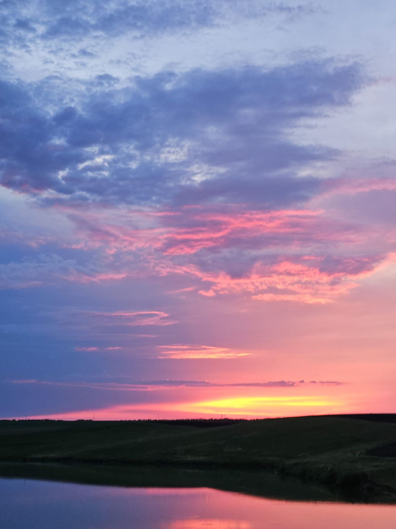 Magenta sunset glowing above rolling fields and a reflective pond