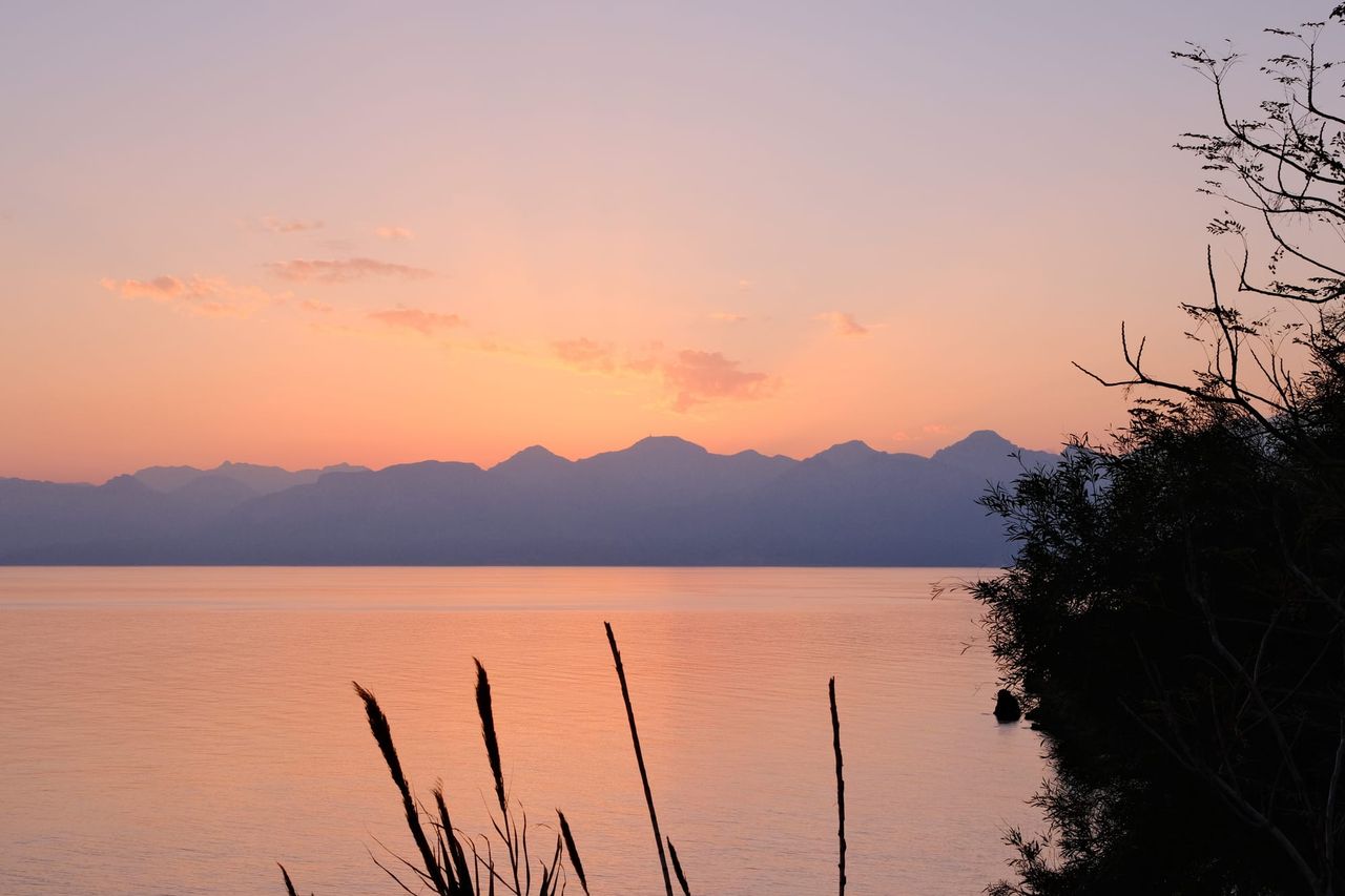 Peach sunset over calm water and distant mountain silhouettes near Antalya