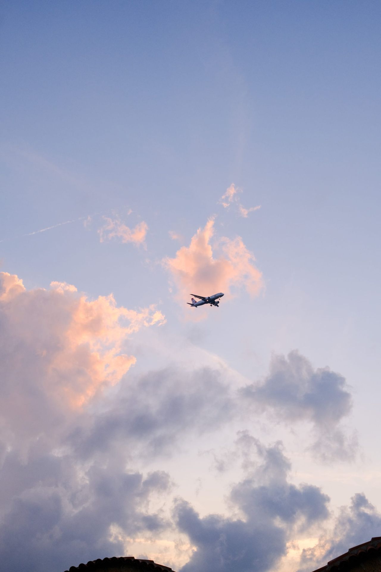 Airplane crossing between softly illuminated clouds in a pale evening sky