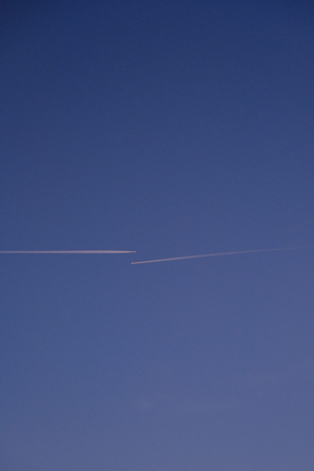 Parallel aircraft trails cutting across a dark blue twilight sky