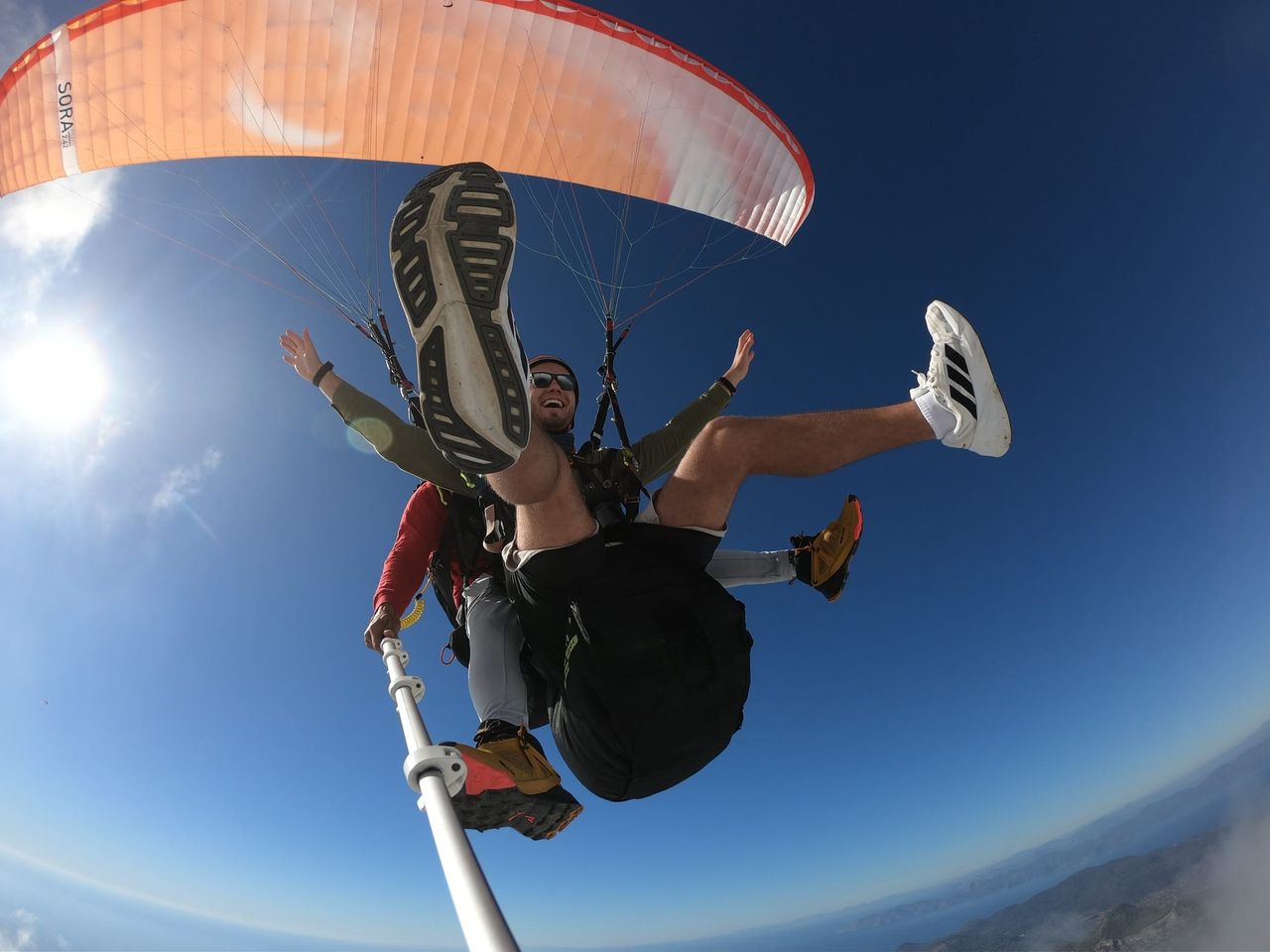 Tandem paragliding pair beneath an orange canopy against blue sky