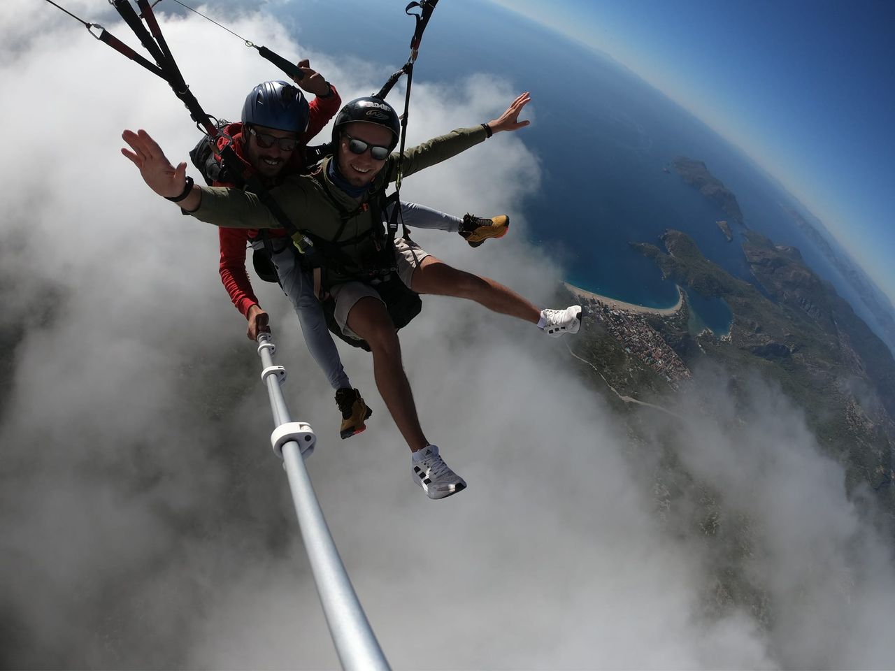 Tandem paragliding pair posing above cloud and coastline