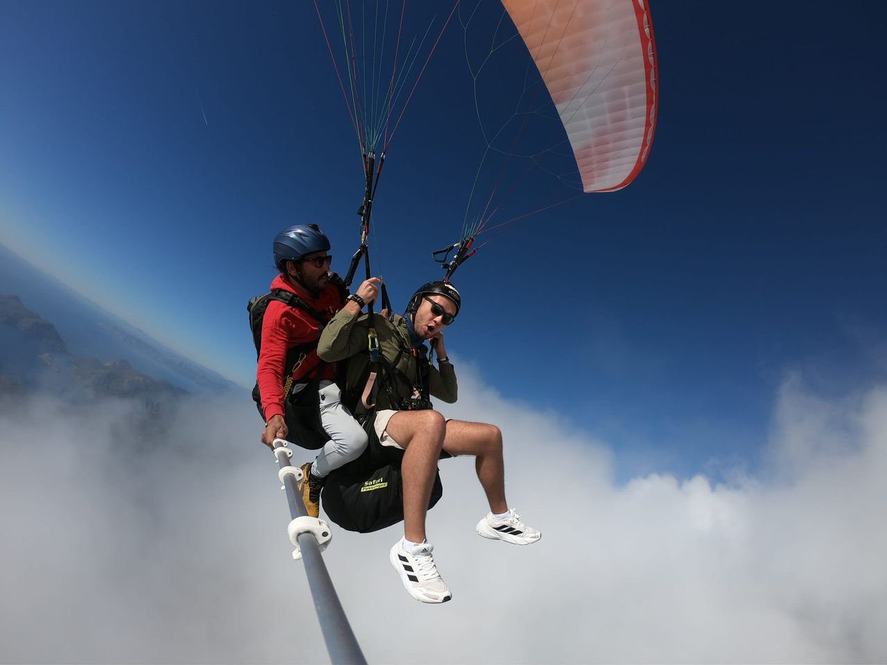 Tandem paragliders gliding along the edge of a bright cloud