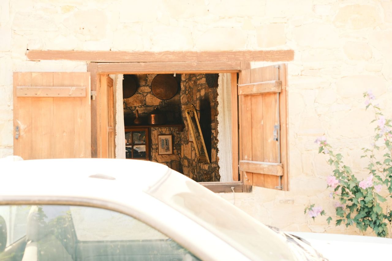 Open wooden shutters on a stone house behind a white car, Cyprus