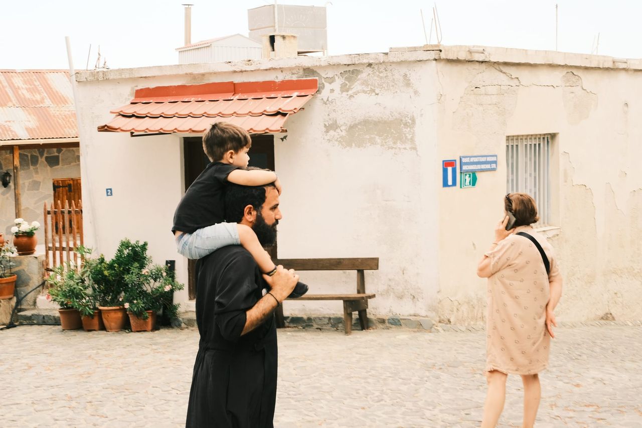 Man carrying a child on his shoulders outside a small building, Cyprus