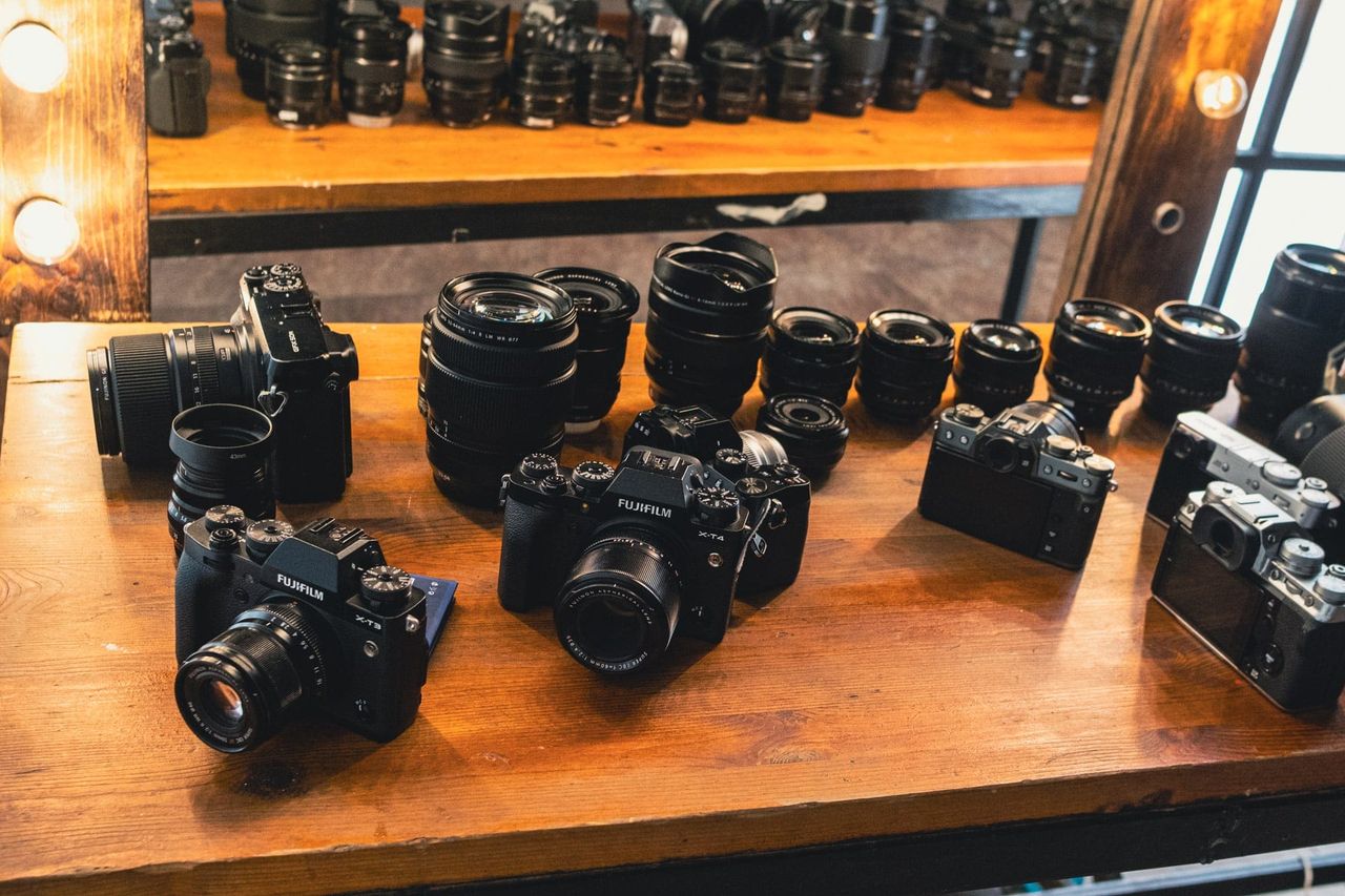 An assortment of cameras and interchangeable lenses arranged on a wooden counter beneath a mirror.