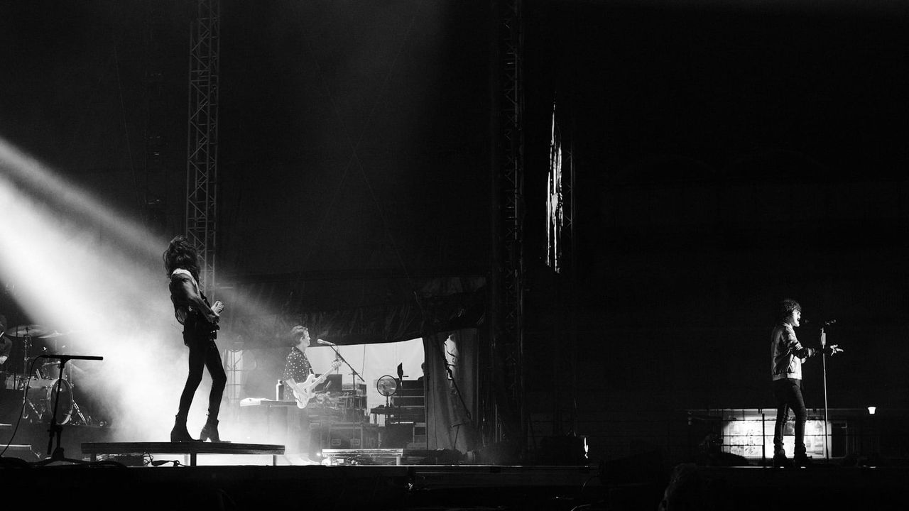 LP and the band performing across a wide stage cut by a bright diagonal spotlight.