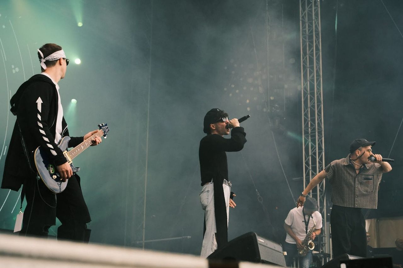 Molec performing with two vocalists, a guitarist and a saxophonist on a hazy festival stage.