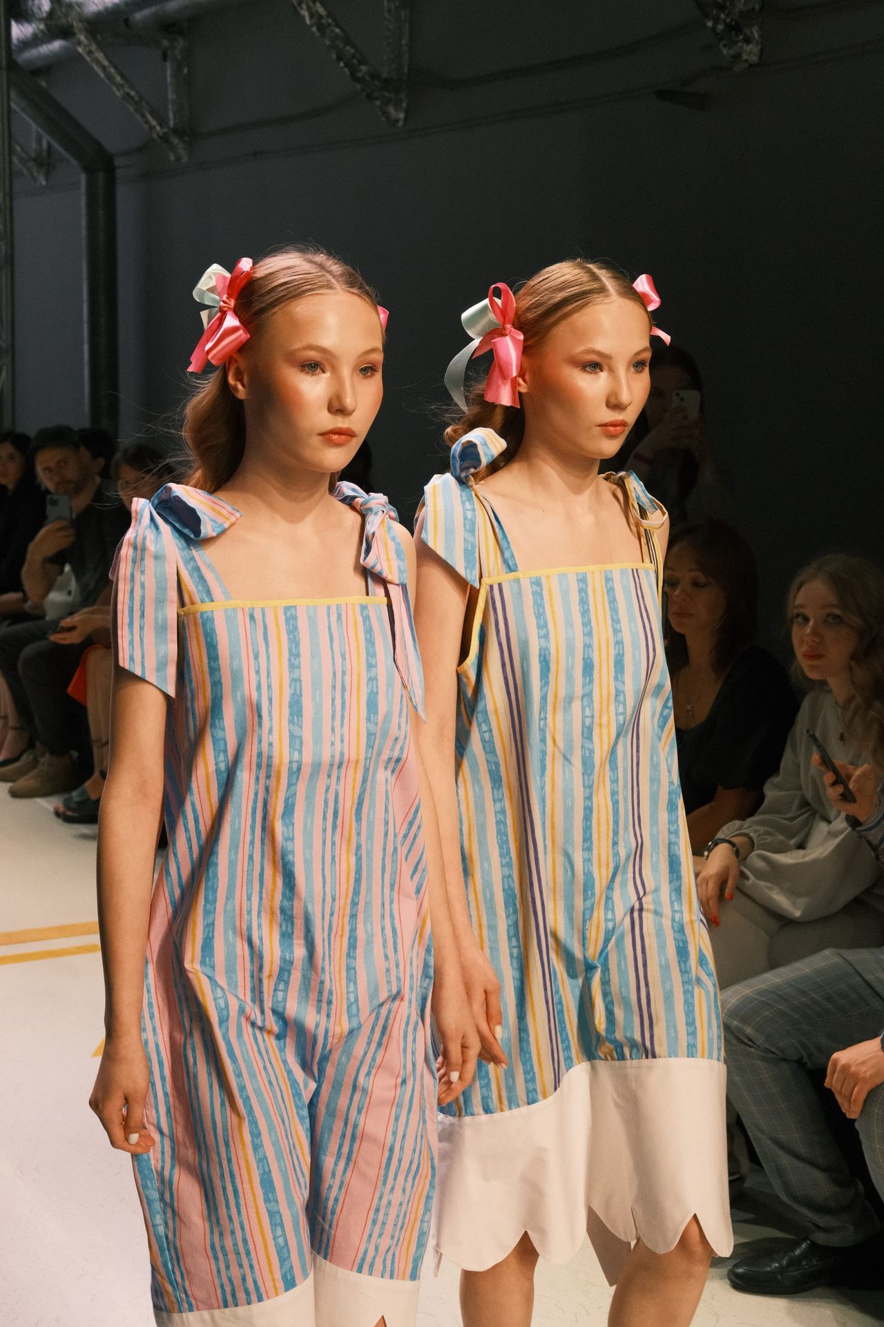 Two models wear pastel-striped dresses with white ruffled hems on the runway.