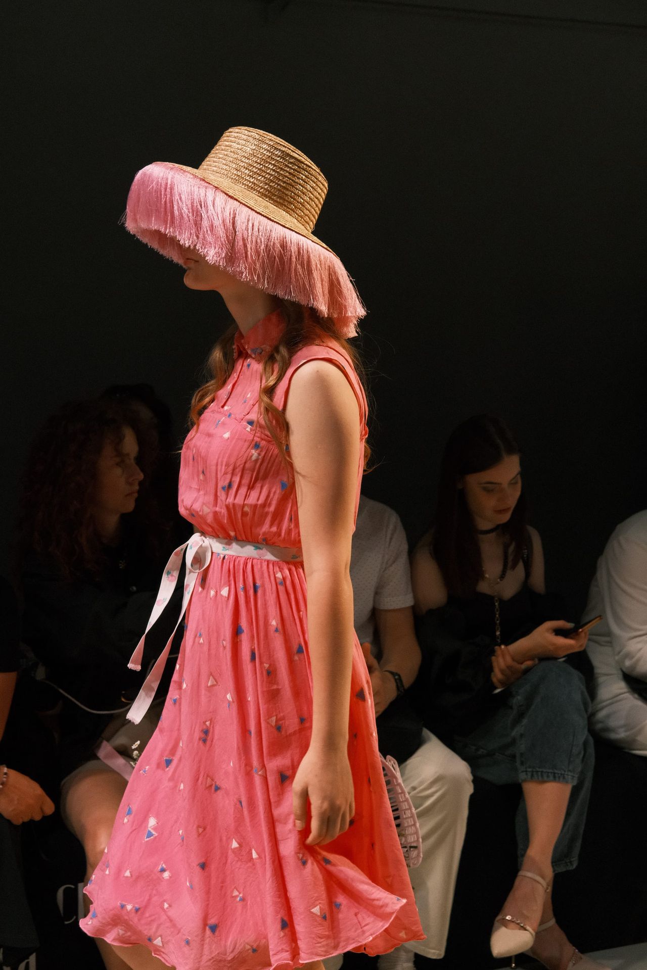 A model walks in a bright pink dress and a wide-brimmed hat with pink trim.