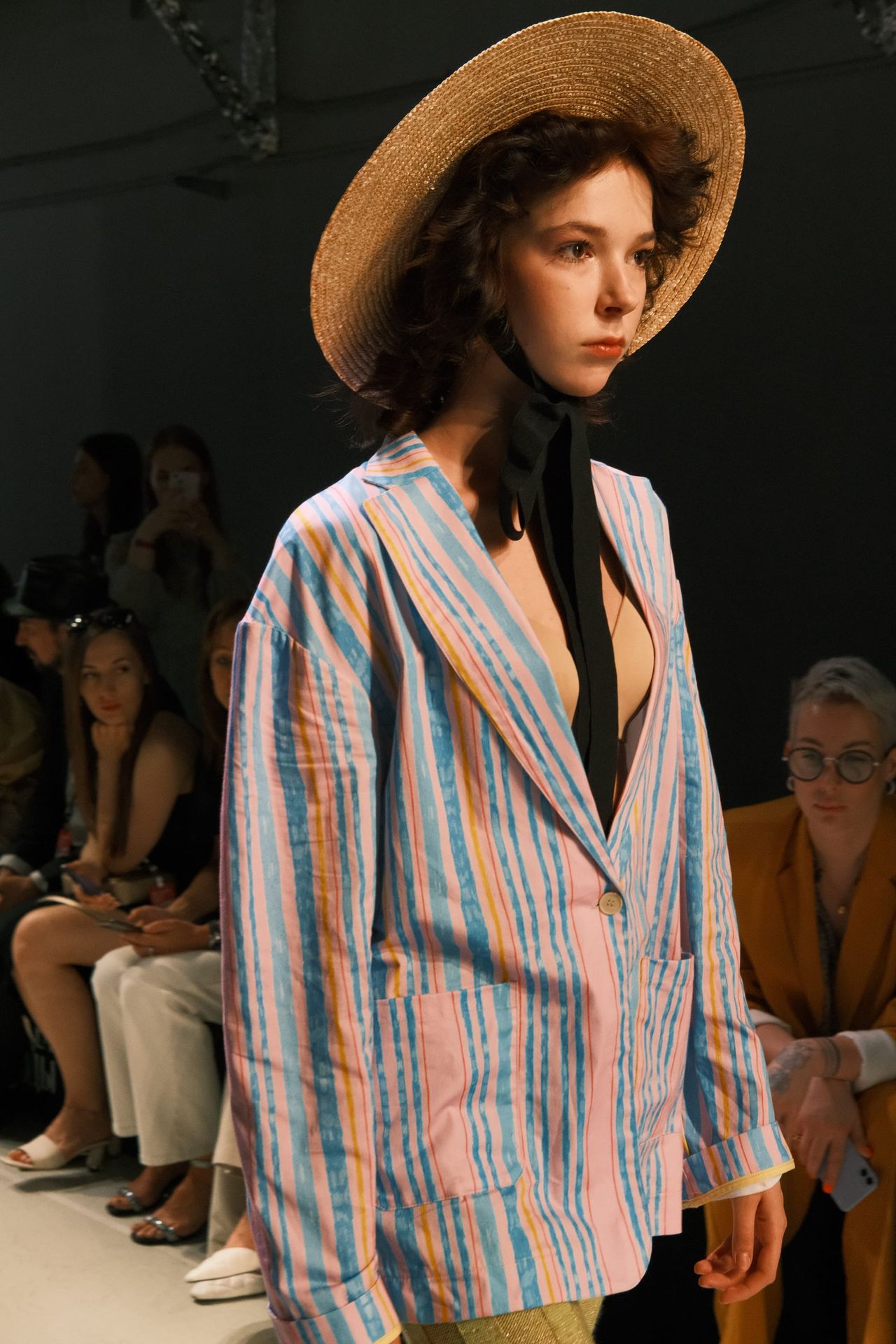 A model in a pastel-striped jacket and shorts wears a straw hat on the runway.