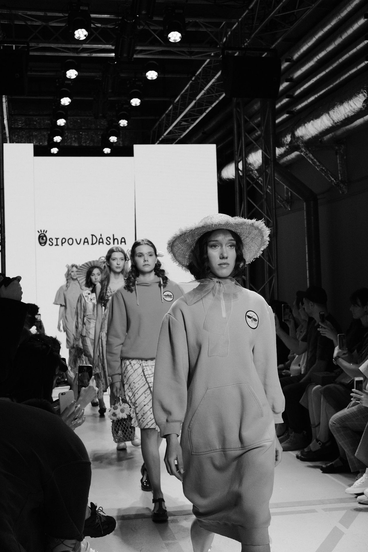 Black-and-white view of models in light outfits walking together along the runway.