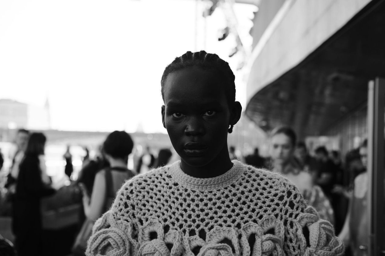 Black-and-white portrait of a model wearing an open-knit top with decorative details.