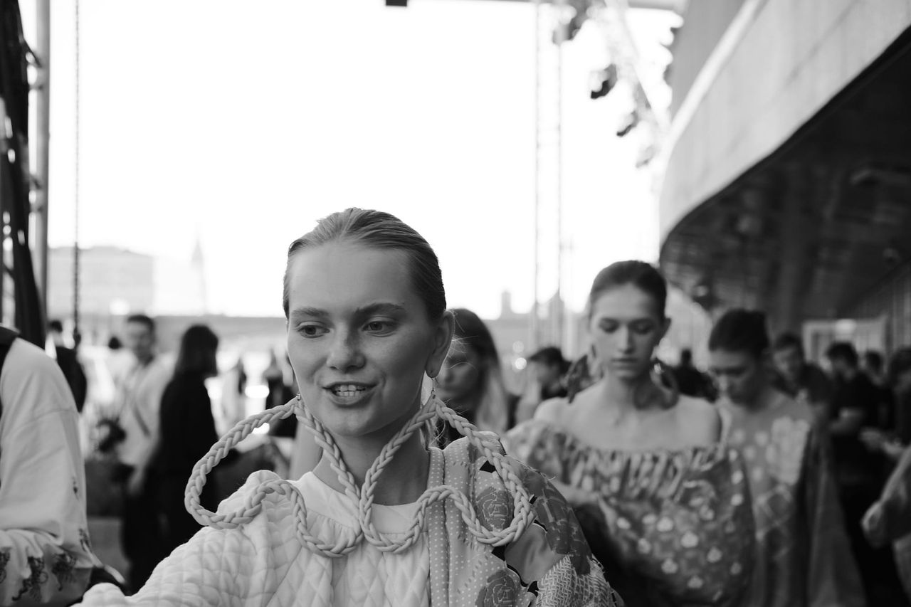 A smiling model wearing oversized loop earrings passes the camera in a black-and-white photograph.