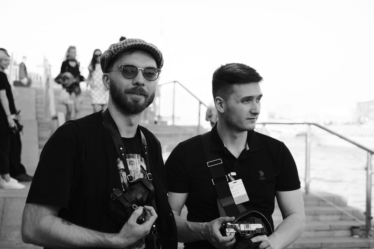 Black-and-white photograph of two men holding cameras near outdoor steps.