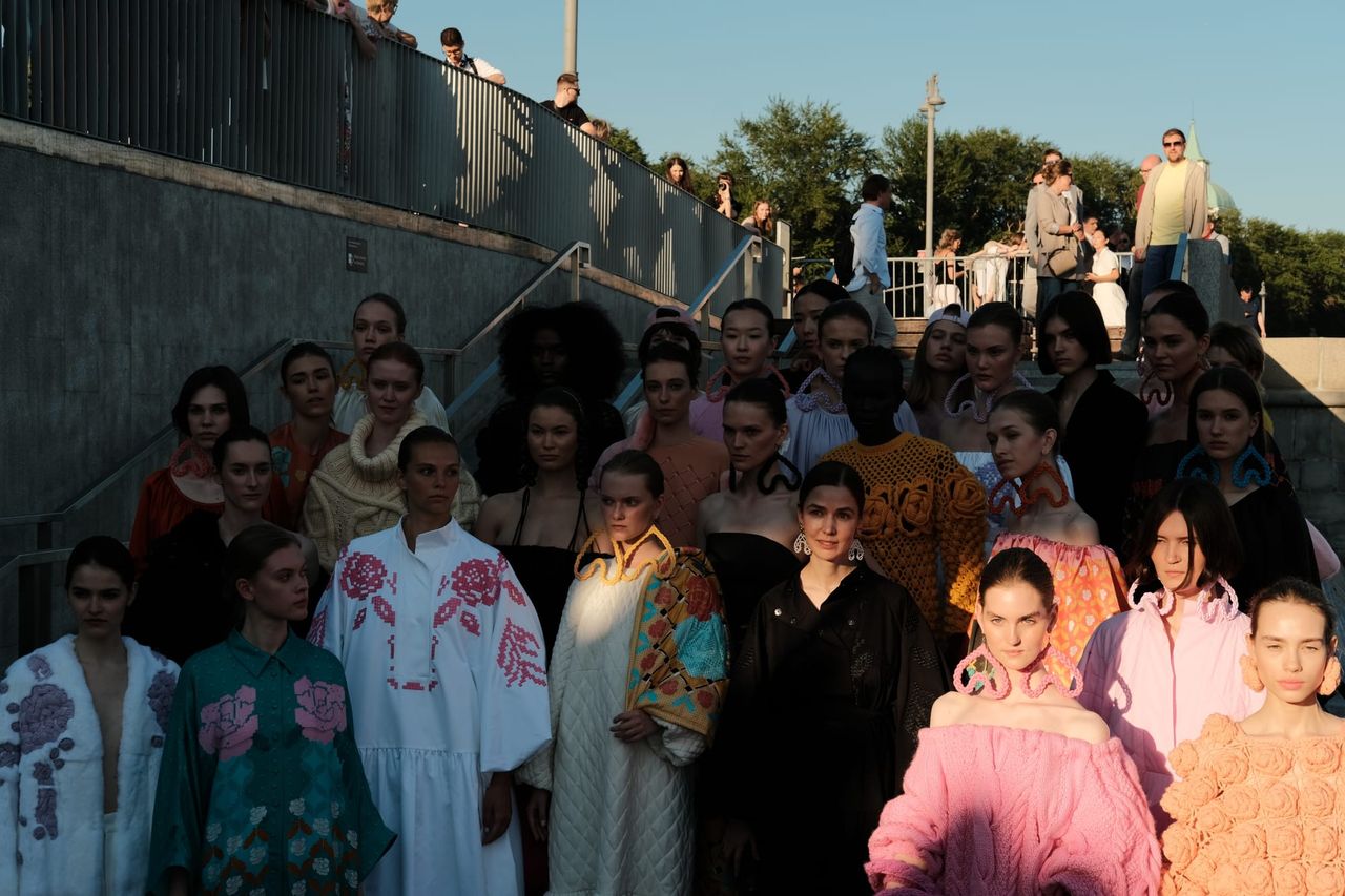 Models in colourful outfits gather on outdoor steps, with sunlight highlighting pink and white ruffles.