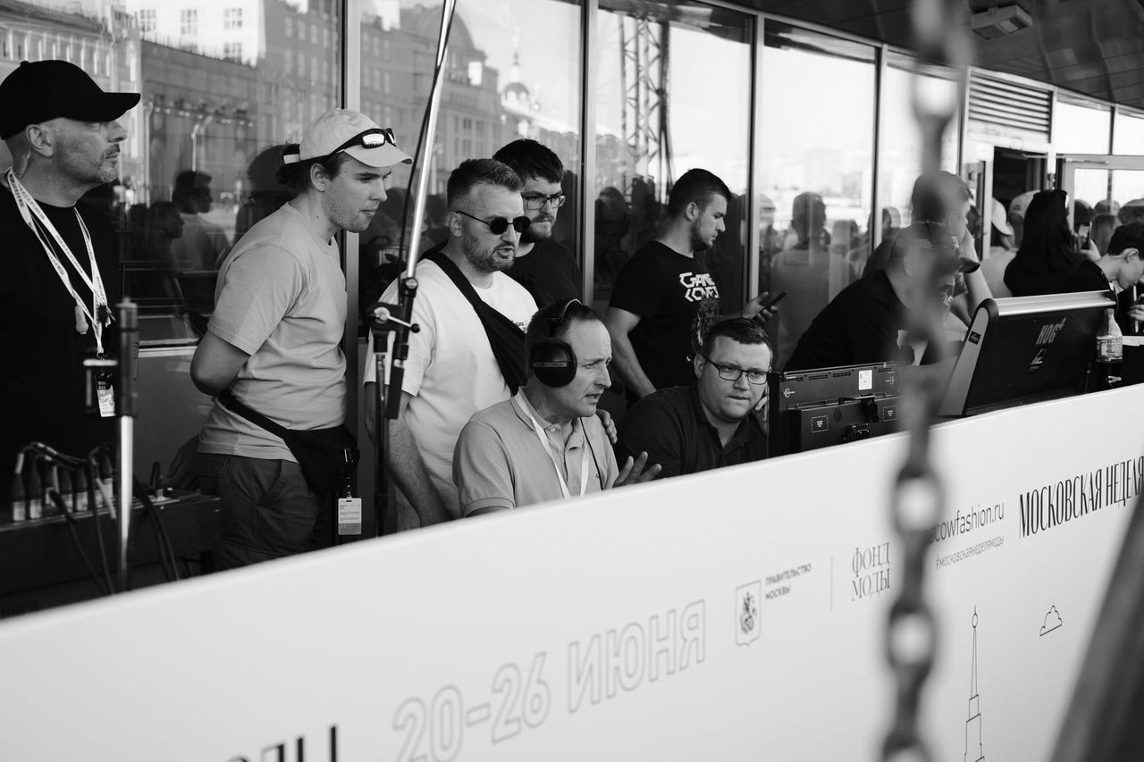 Black-and-white view of photographers and event staff gathered behind a branded barrier.
