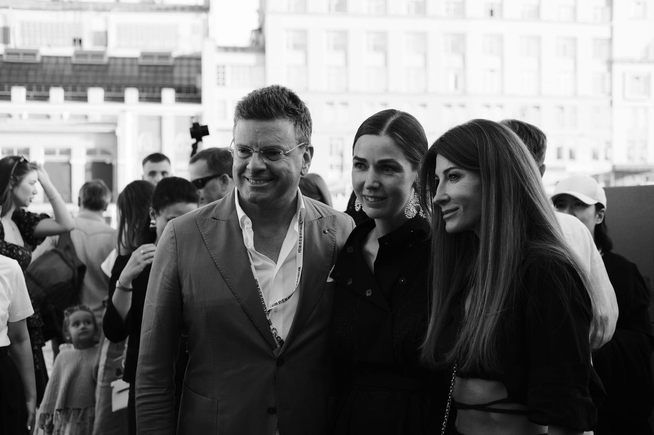 A man and two women smile for a photograph among the outdoor crowd, in black and white.