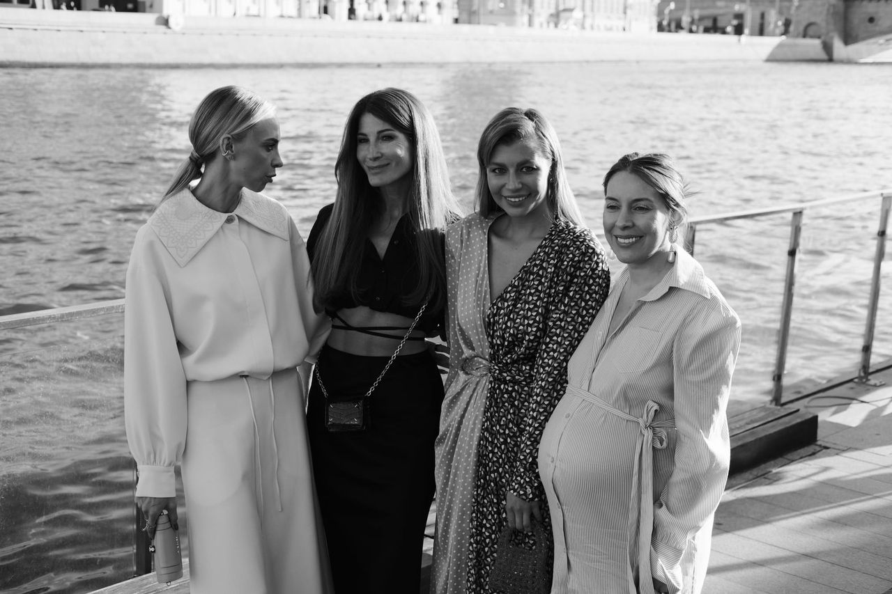 Four women pose together beside the river in a black-and-white photograph.