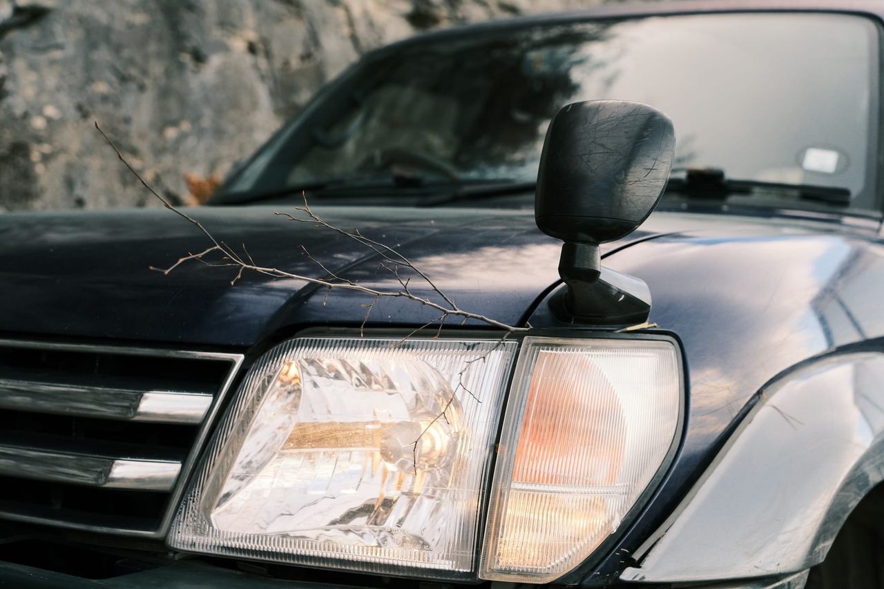 Close view of a Toyota’s headlight, grille and wing mirror beside a rocky slope.