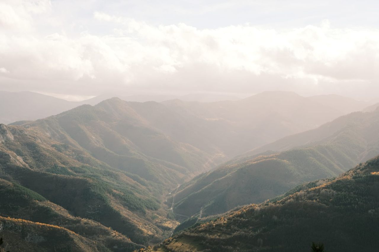 Panoramic view of wooded mountain ridges receding into soft golden light.