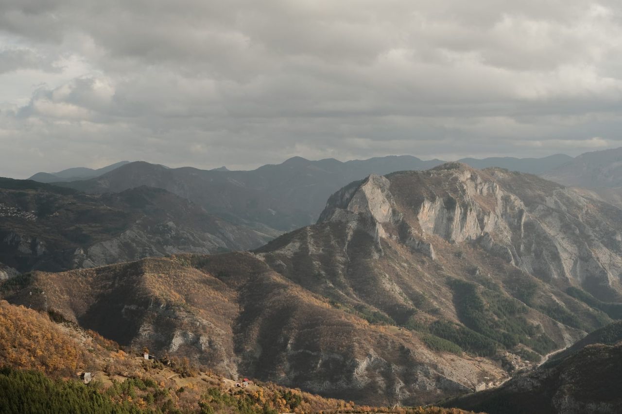A pale, steep-sided mountain rises beneath dark clouds above surrounding forested ridges.