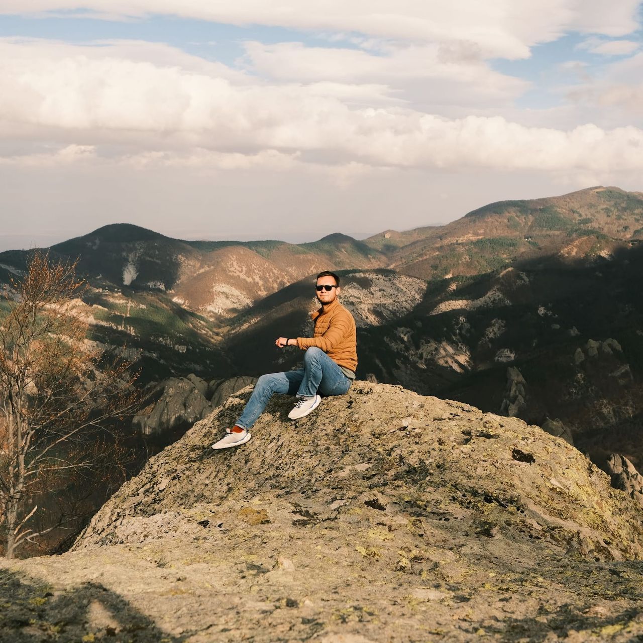 A person rests on a rocky summit with mountain ridges extending behind them.