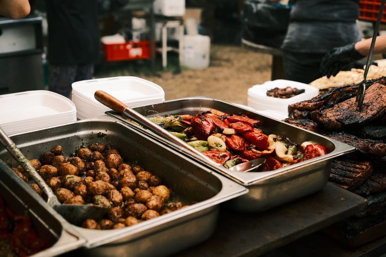 Serving trays hold cooked mushrooms and colourful grilled vegetables beside the barbecue.