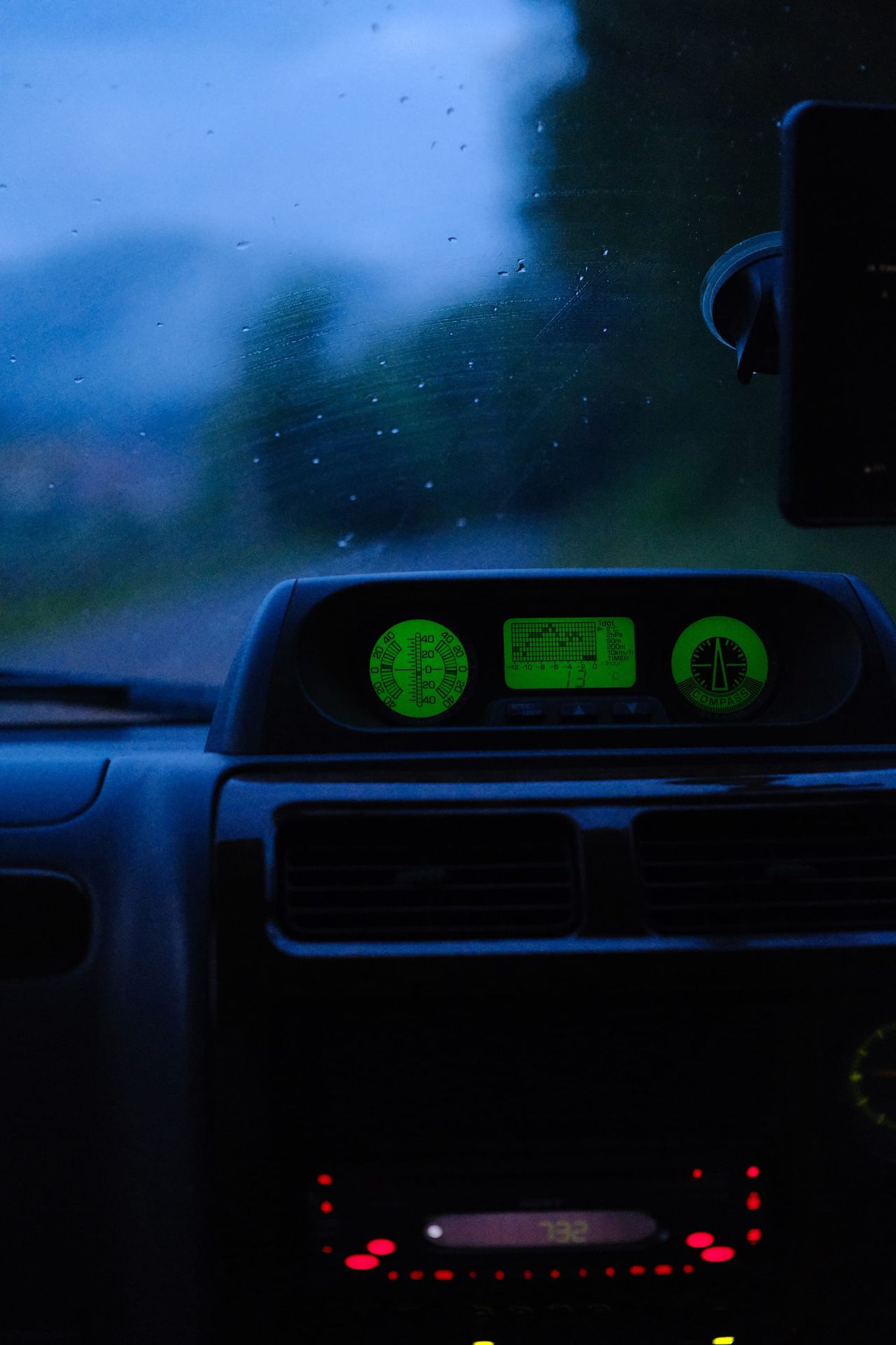 Car dashboard glowing green during a rainy twilight drive