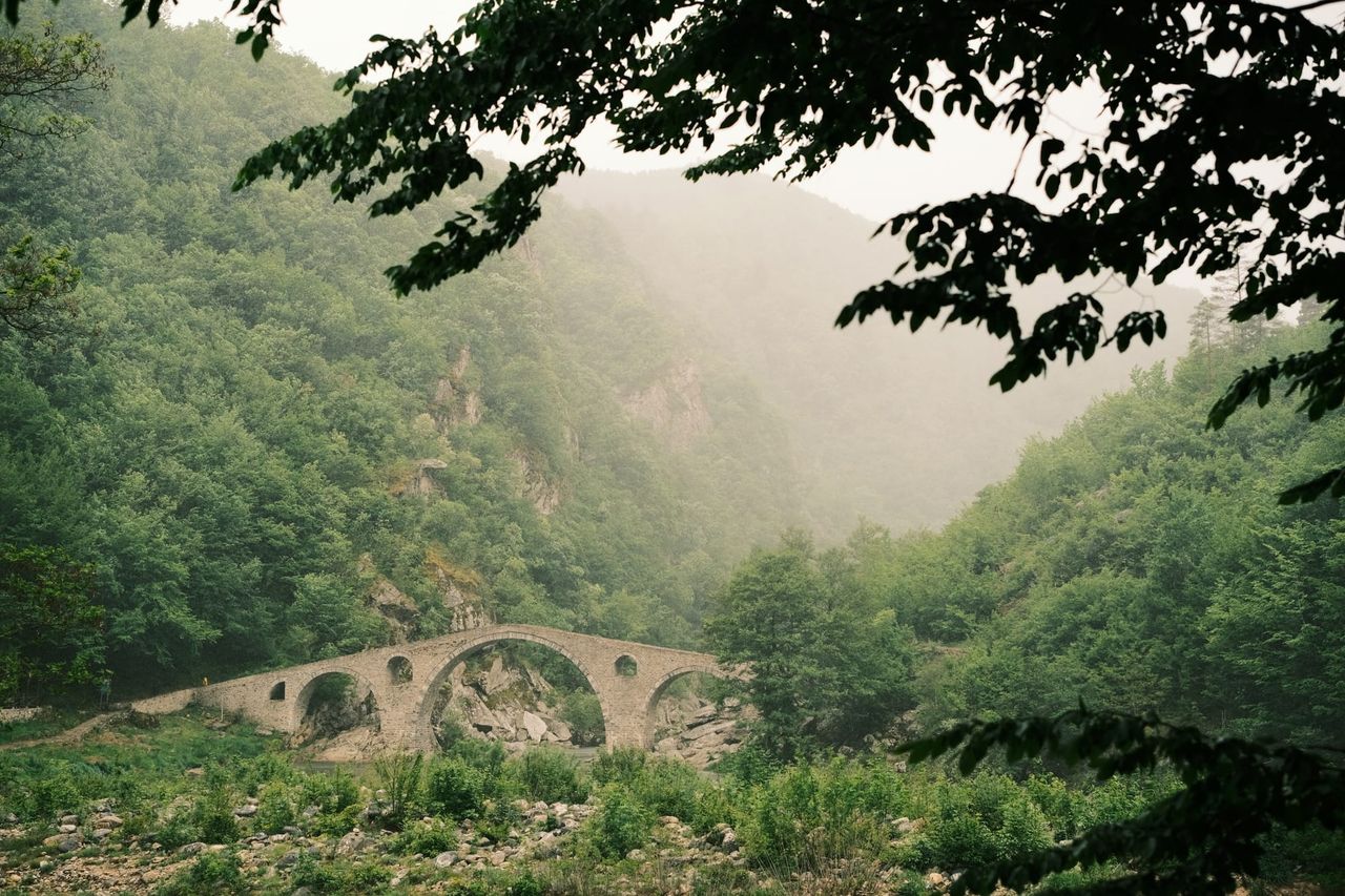 Stone arch bridge over a river below misty wooded slopes, Bulgaria