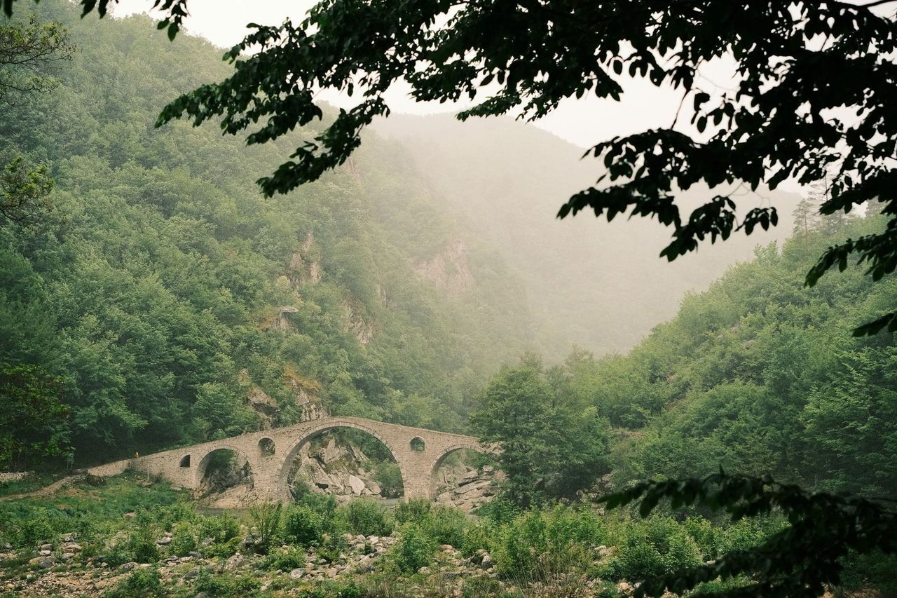 Stone arch bridge over a river below misty wooded slopes, Bulgaria