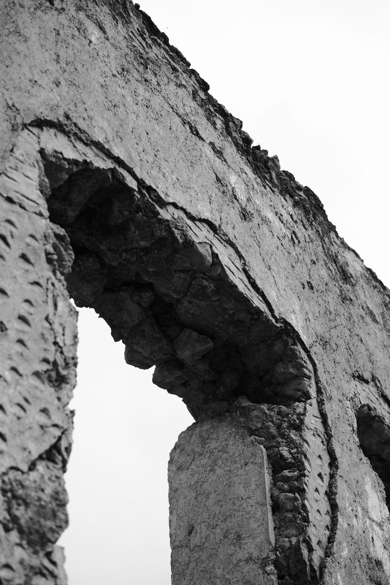 Black-and-white close view of a crumbling stone arch in Kayaköy