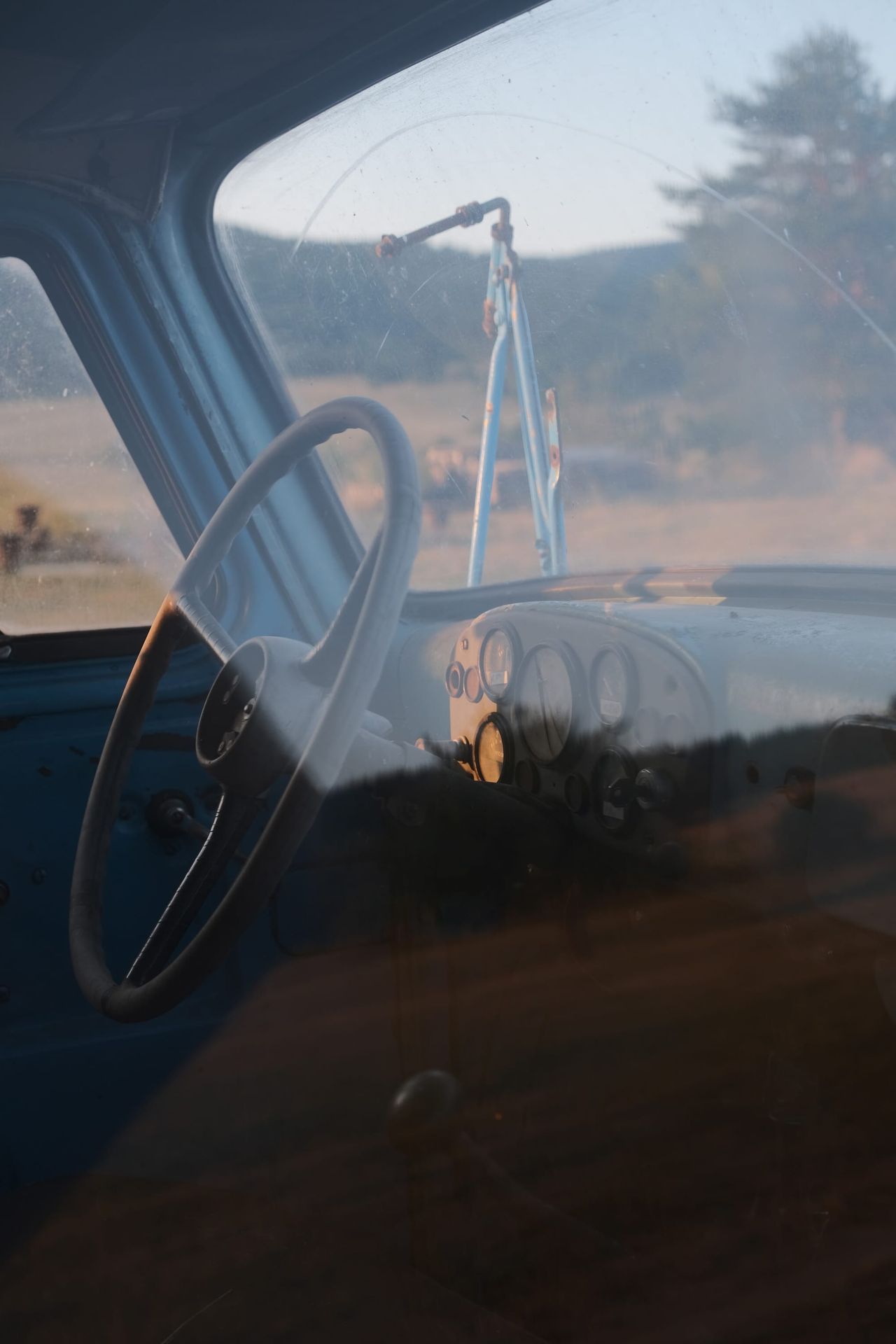 Steering wheel visible through an old truck window reflecting the landscape beside Batak Lake.