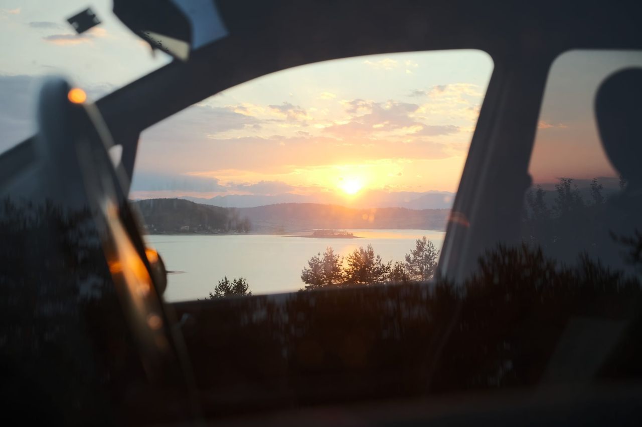 Sunset over Batak Lake framed by car windows and dark interior details.