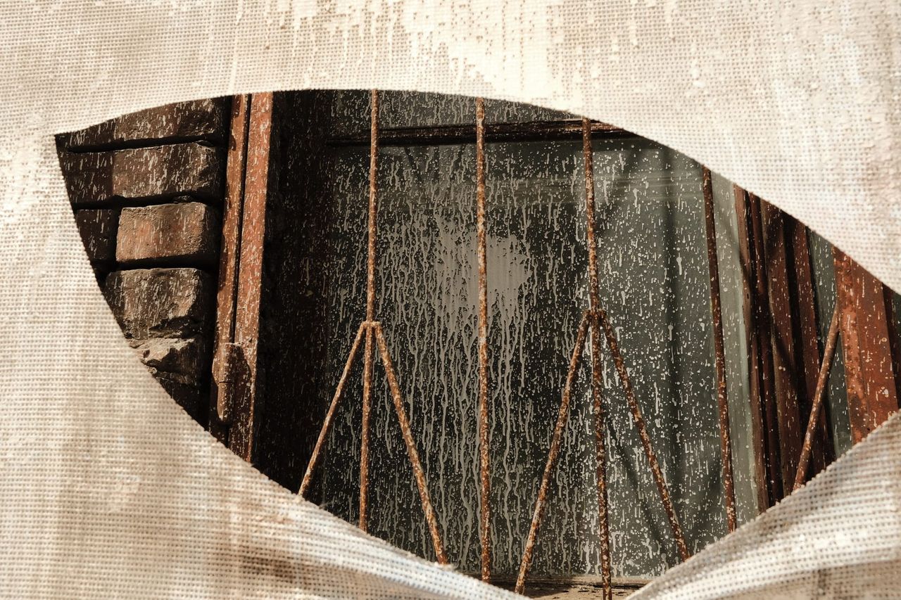 Torn white mesh reveals rusted metal bars and a dark window set in brickwork in Moscow.