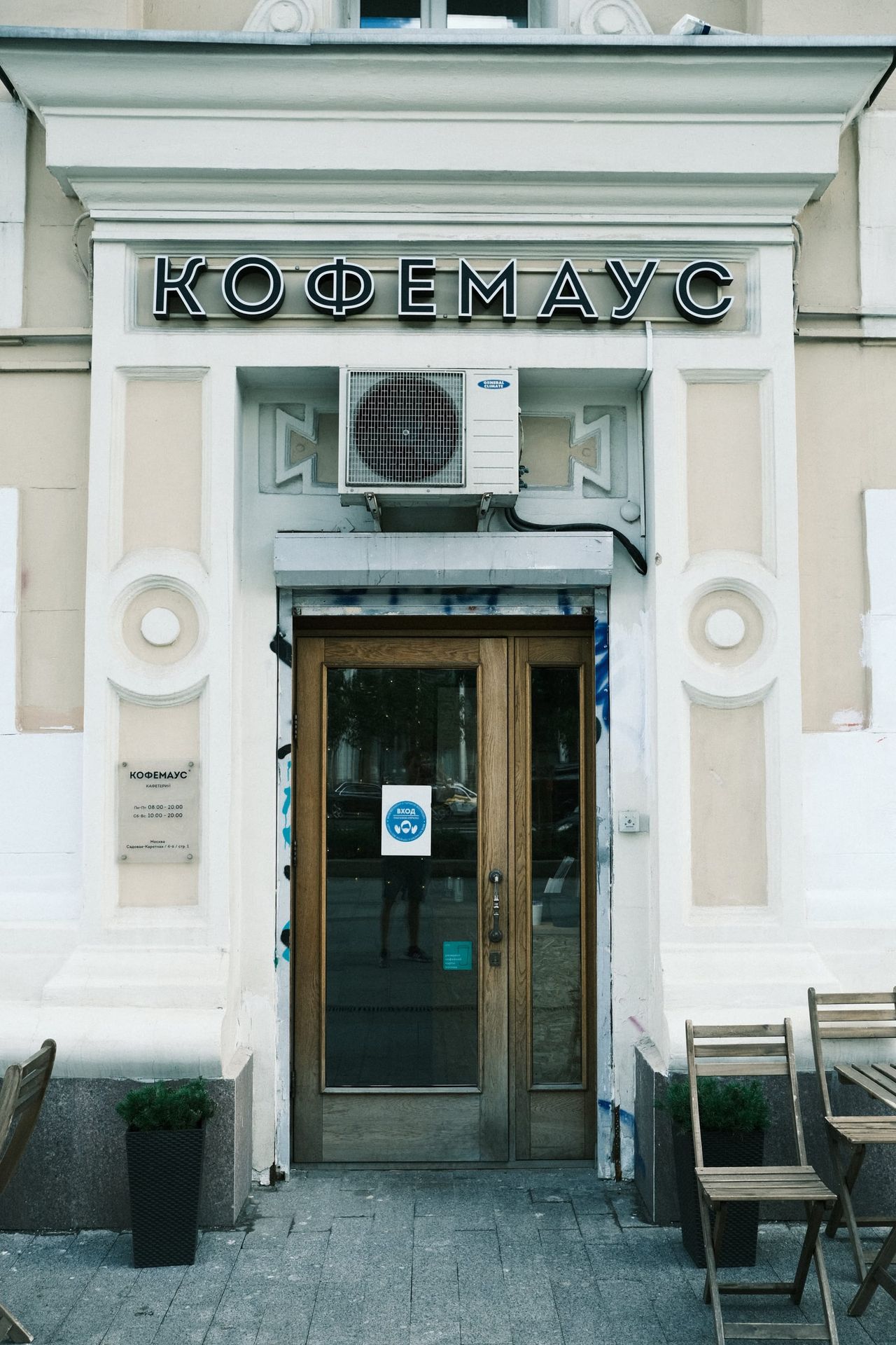 A cafe doorway beneath a Cyrillic sign and an air-conditioning unit on a pale Moscow facade.