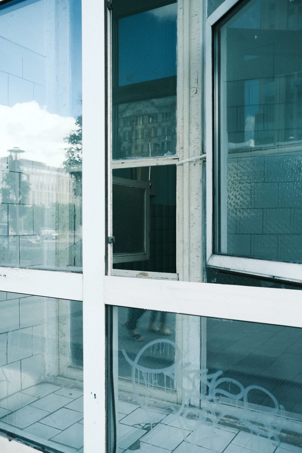 Buildings and sky reflected in white-framed windows beside an open section covered with silver material in Moscow.