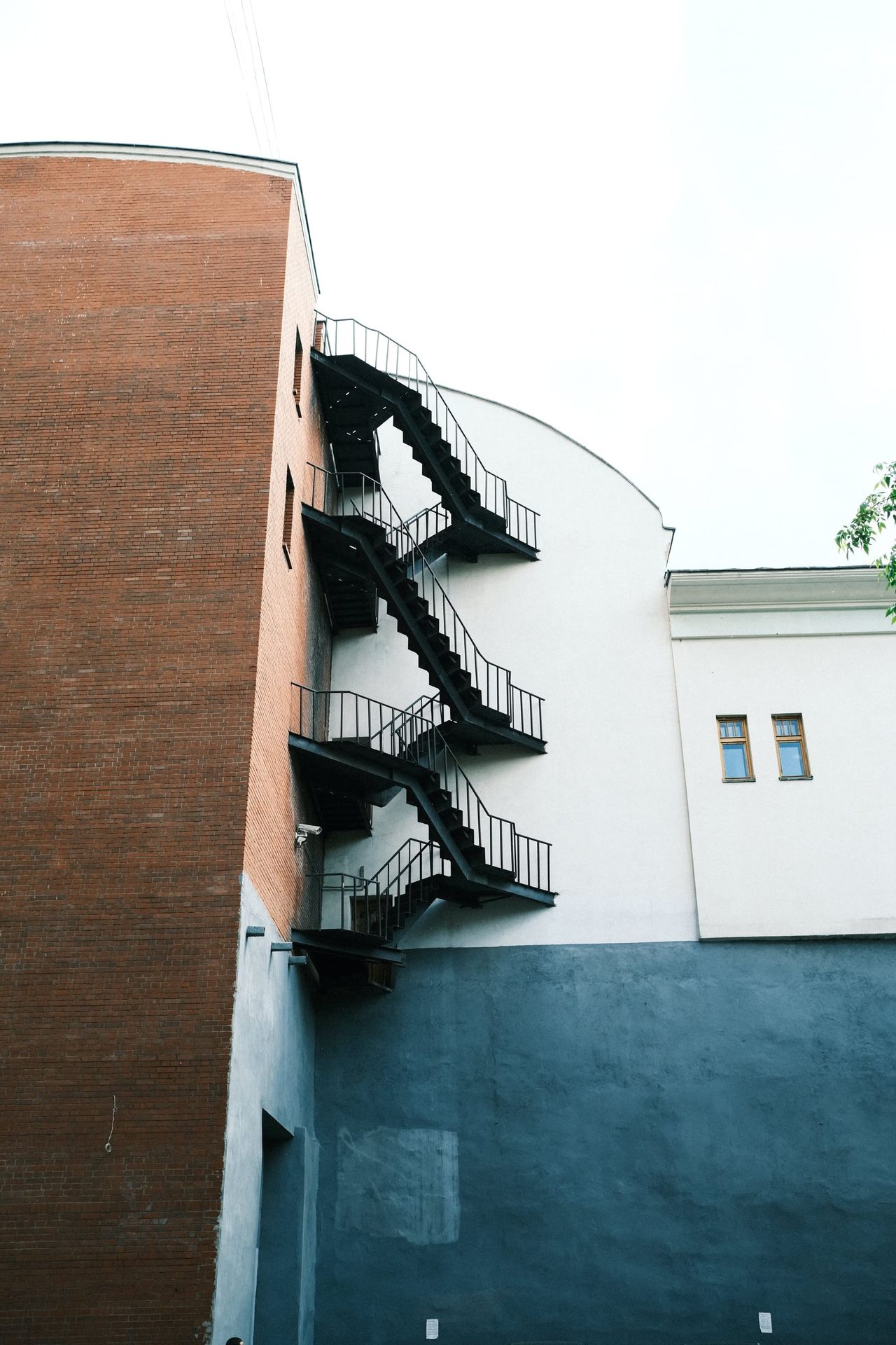 A black exterior fire escape zigzags between a red brick wall and a curved white facade in Moscow.