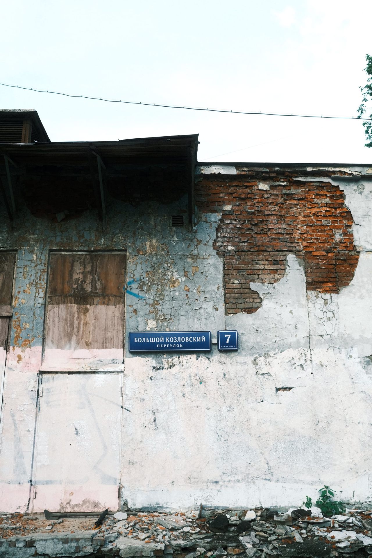 A blue street-number plate sits on a weathered white wall with exposed red brick and a boarded opening in Moscow.